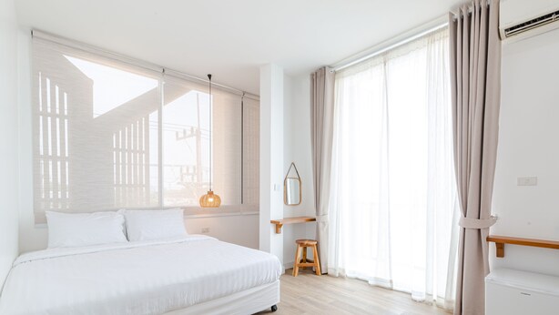 Habitació d'hotel moderna amb un llit gran, un sòl de fusta, un petit tamboret i una finestra amb cortines.