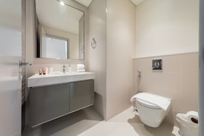 A modern bathroom with a marble countertop, a toilet, and a large mirror.
