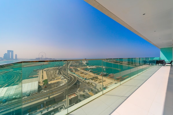 A high-rise building with a glass floor offering a view of a coastal cityscape, including a marina and urban development.