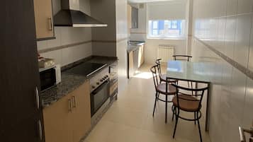 A modern kitchen with a dining area, featuring a granite countertop, stainless steel appliances, and a glass dining table with four chairs.