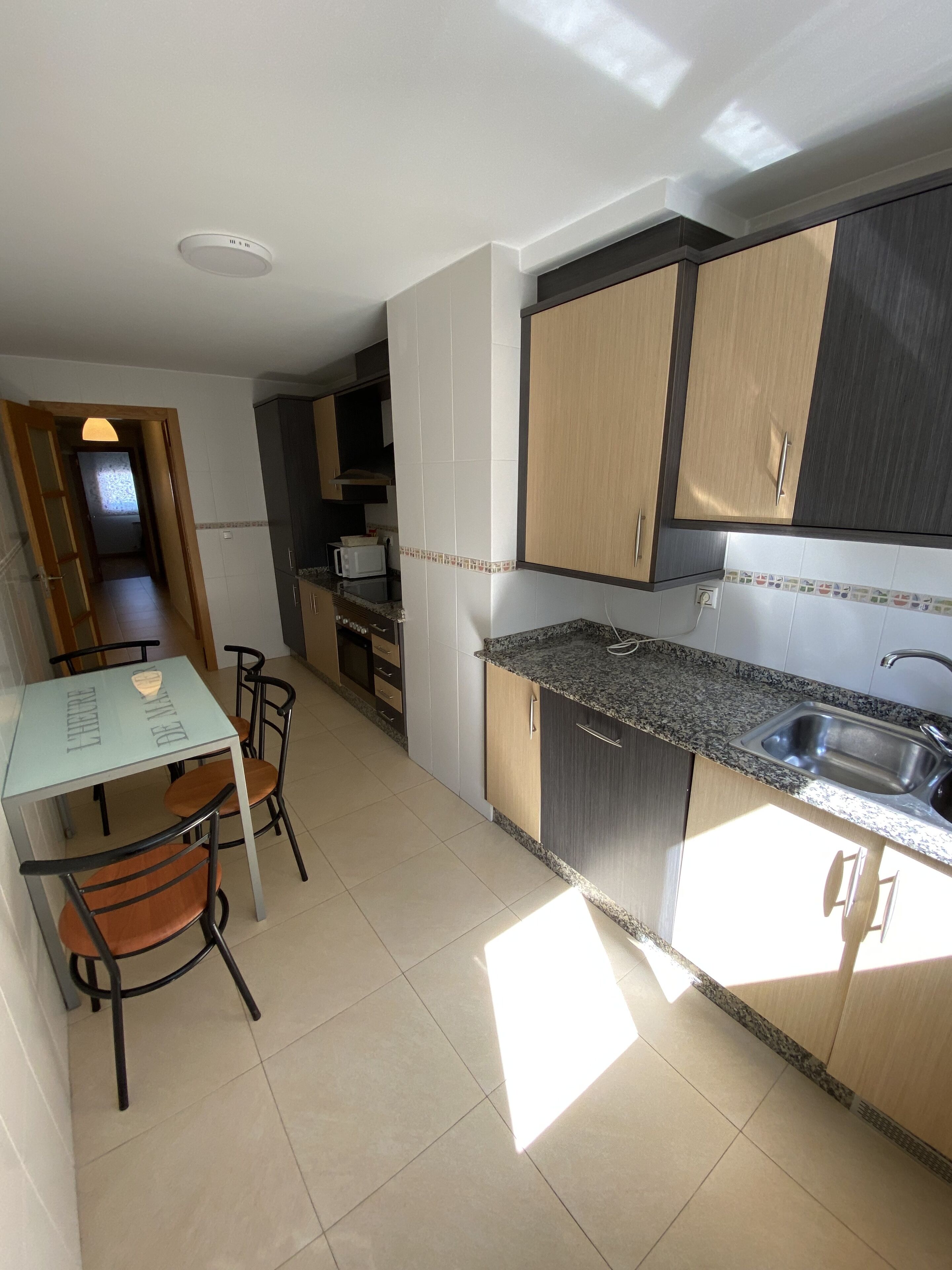 A modern kitchen with a dining area, featuring a granite countertop, stainless steel sink, and wooden cabinets.