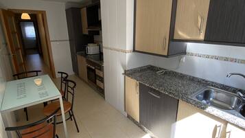 A modern kitchen with a dining area, featuring a granite countertop, stainless steel sink, and wooden cabinets.