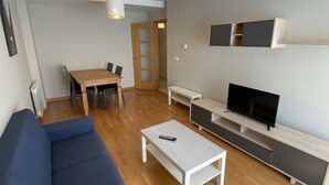 A modern living room with a blue sofa, a wooden dining table, a TV on a wooden stand, and a ceiling light fixture. - dpCristal Calvo Sotelo 164 4C (Sarria)