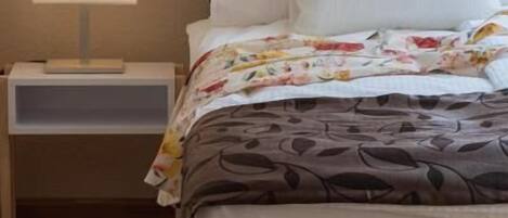 A neatly made bed with a floral duvet, a bedside lamp, and a wooden floor.
