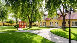 A well-maintained courtyard with a paved walkway, a red gazebo, and a yellow building with a red roof. - Budapest Airport Eprespark Hotel (Vecsés)
