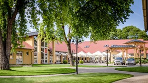 A hotel with outdoor seating, a red roof, and a paved walkway. - Budapest Airport Eprespark Hotel (Vecsés)