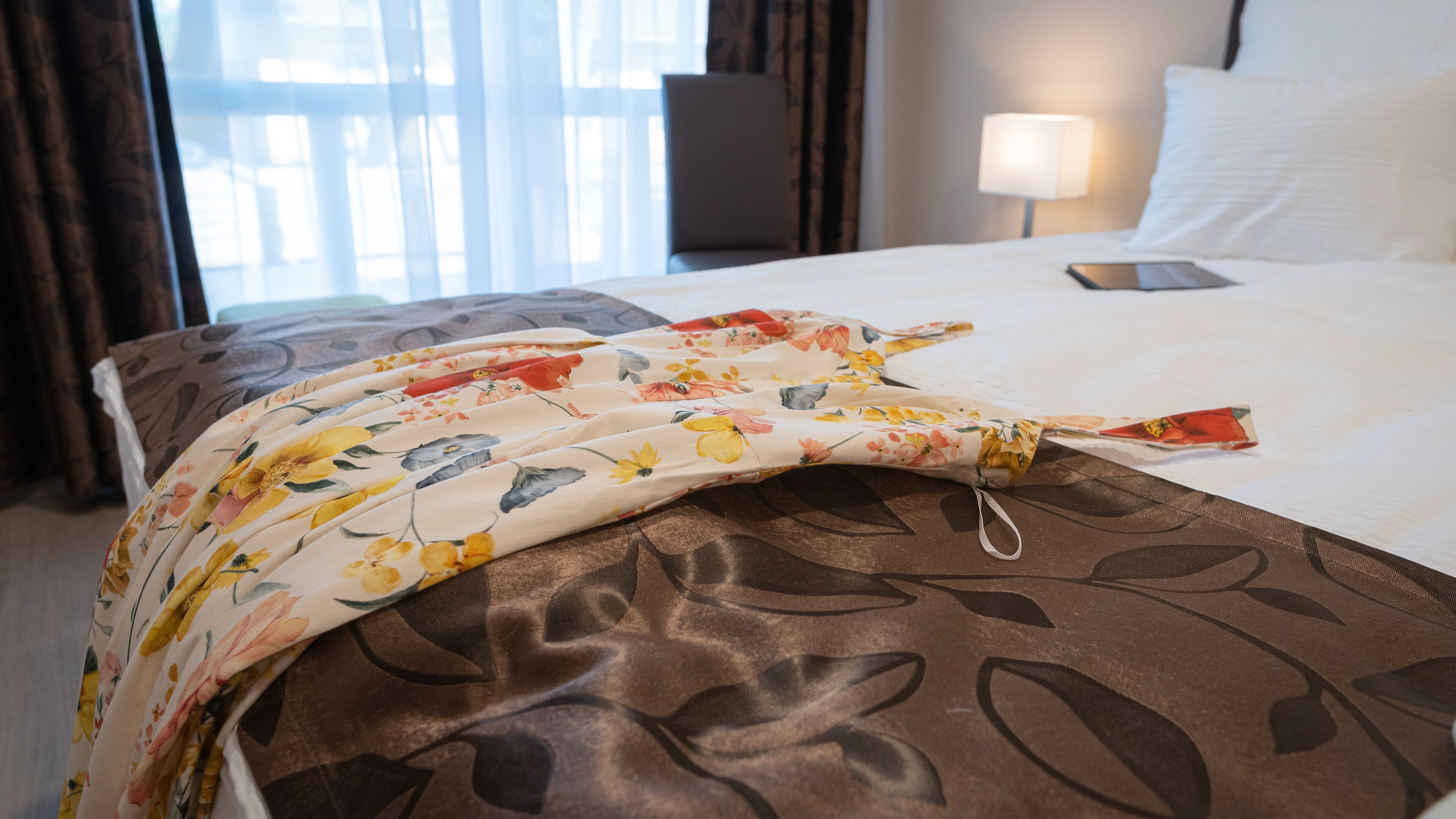 A hotel room with a bed, a lamp, and a smartphone on the bed.