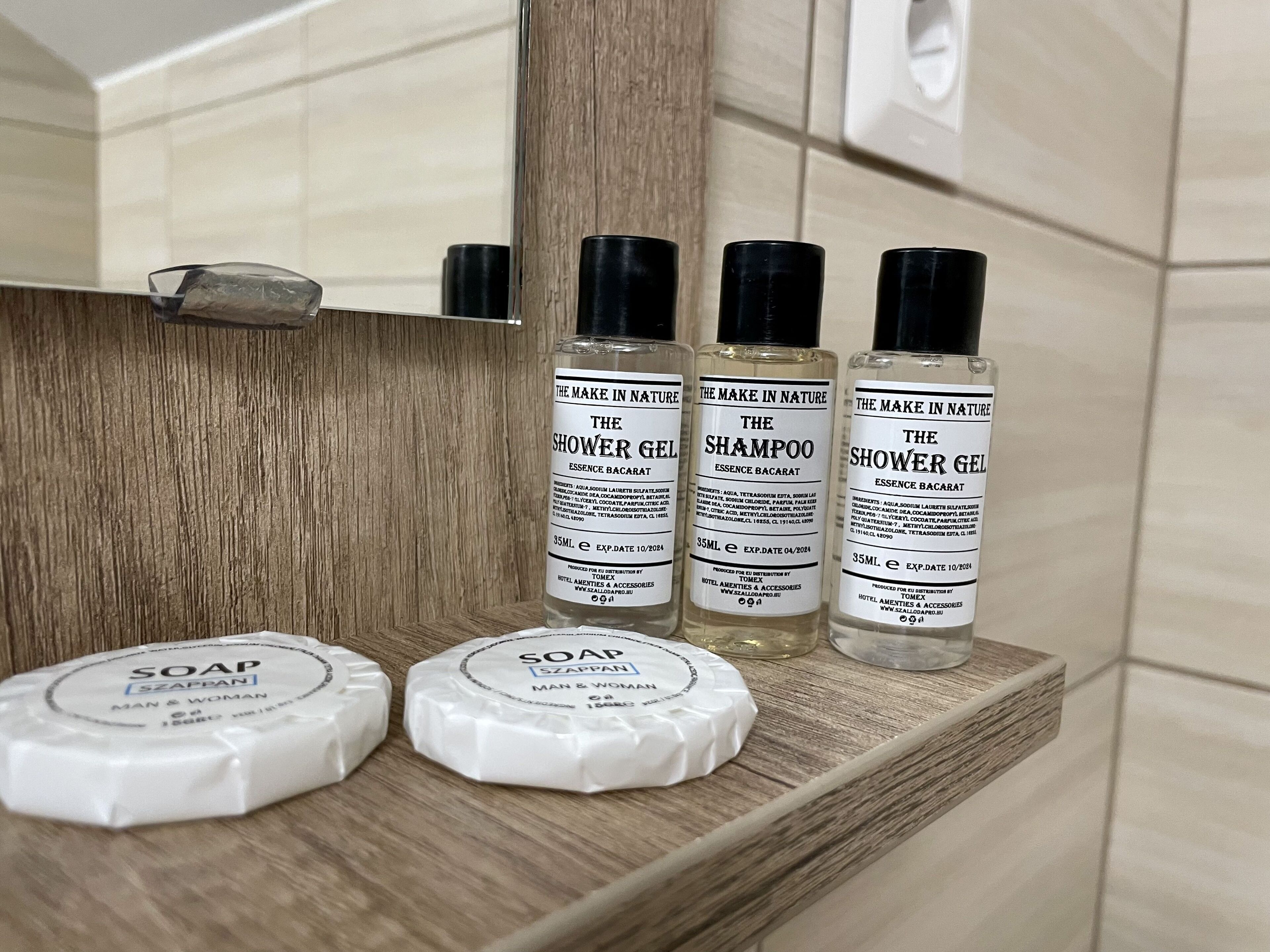 A bathroom shelf with three bottles of shower gel and shampoo, and two bars of soap.