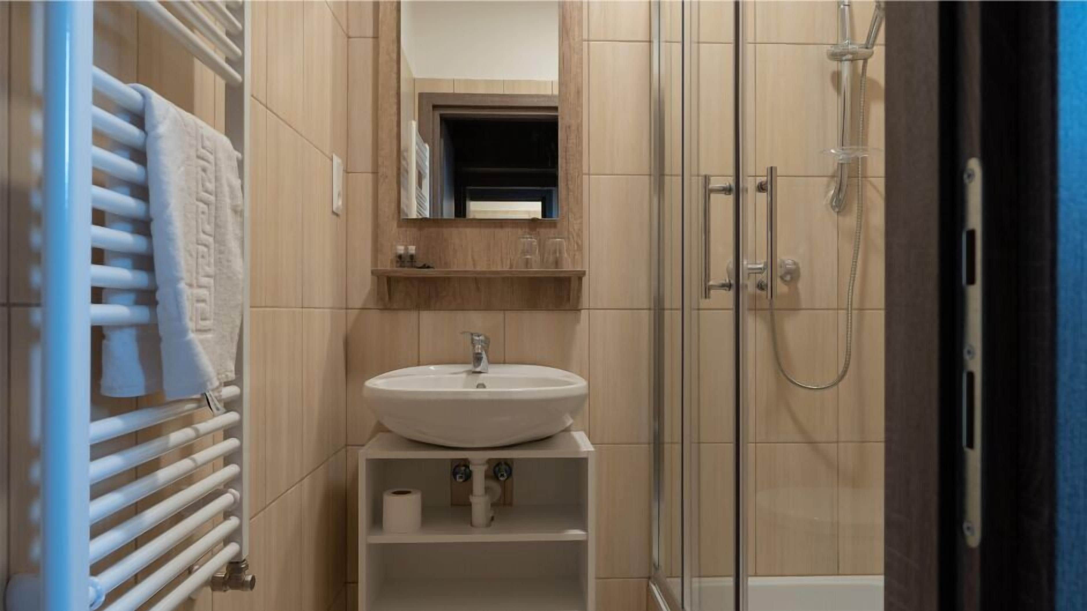 A bathroom with a white sink, a mirror above it, a towel rack, and a shower area.