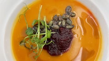 Ein weißer Teller mit einem Gericht, das Fleisch, Blattgemüse und Samen in einer gelben Soße enthält.