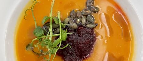 A white plate with a dish containing a piece of meat, some greens, and seeds in a yellow sauce.