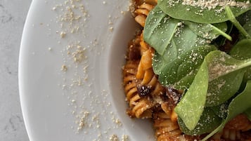 A white plate with pasta, spinach, and crumbs.