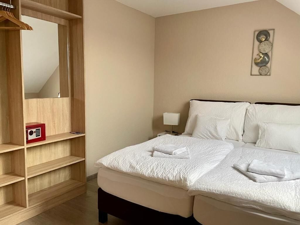 A hotel room with a bed, a wooden wardrobe, a bedside table with a lamp, and a wall art piece.