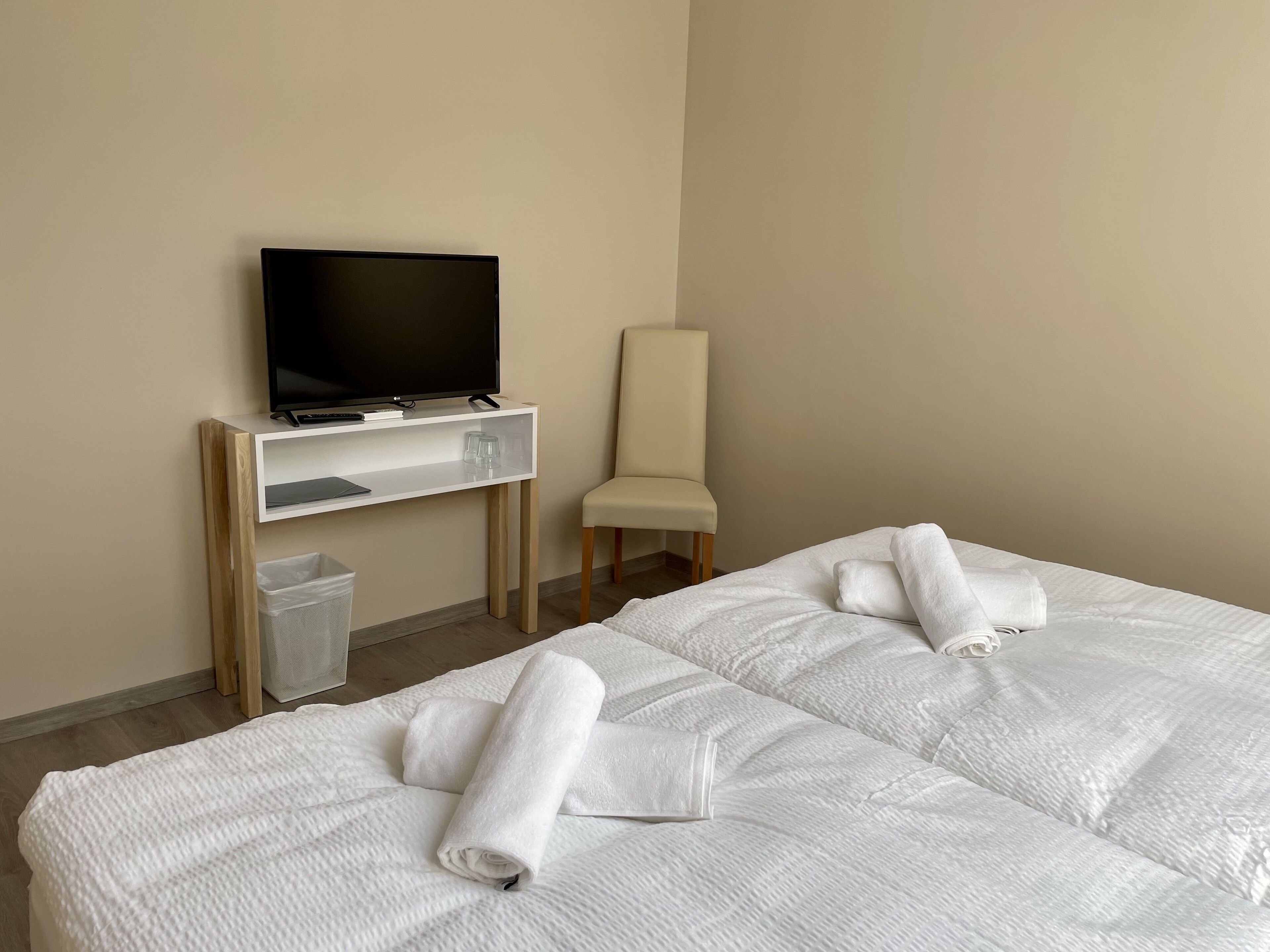 A hotel room with two beds, a TV on a stand, a chair, and a trash bin.