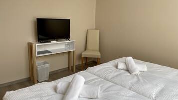 A hotel room with two beds, a TV on a stand, a chair, and a trash bin.