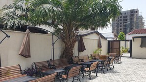 An outdoor seating area with wooden benches and tables, surrounded by a low wall and a palm tree. - Nicotel (Lekki)