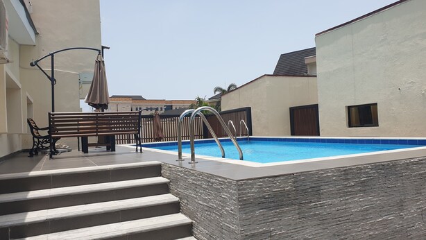 A swimming pool with steps leading up to it, a bench, and a fence. - Nicotel (Lekki)