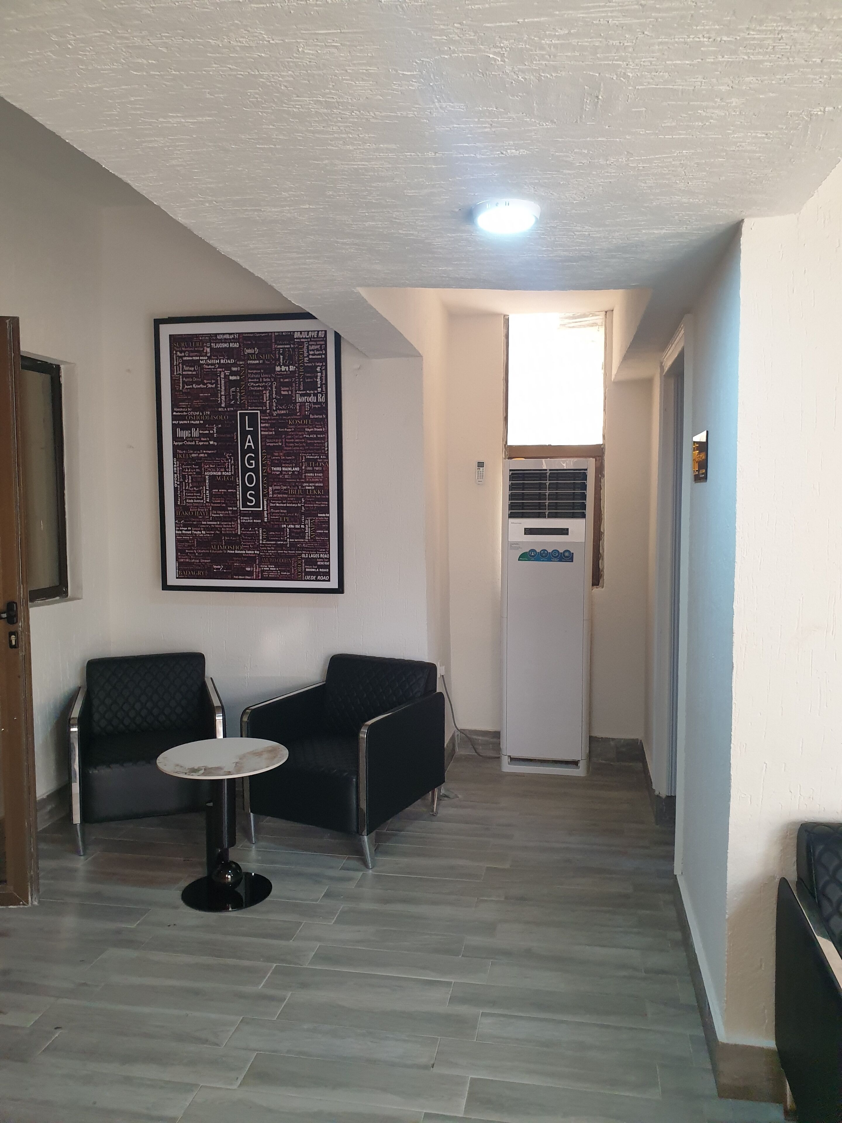 A hallway with a seating area featuring two black cushioned chairs and a small round table. A map of Lagos is displayed on the wall.