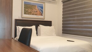 A hotel room with a bed, a desk, a chair, a picture on the wall, and a window with blinds. - Nicotel (Lekki)