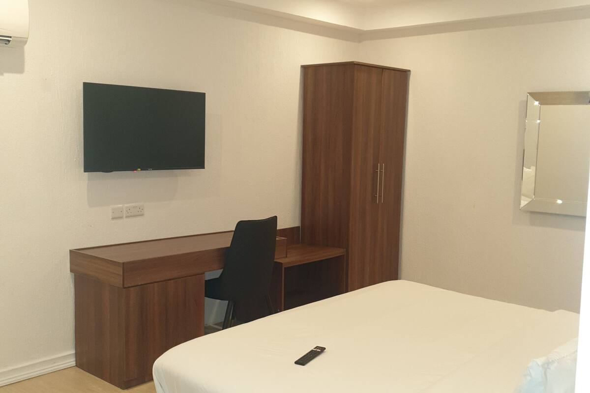 Ein Hotelzimmer mit einem Bett, einem Schreibtisch, einem Stuhl, einem an der Wand befestigten Fernseher und einem Kleiderschrank.