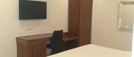 A hotel room with a bed, a desk, a chair, a TV mounted on the wall, and a wardrobe.