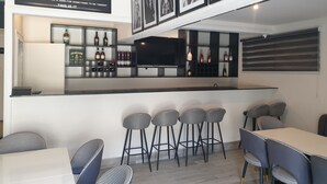 A modern bar area with a counter, bar stools, and a television. There are framed pictures on the wall and a sign above the bar. - Nicotel (Lekki)