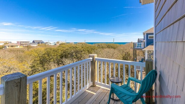 A wooden deck with a white railing, a turquoise chair, and a small table.