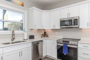 A modern kitchen with white cabinetry, a stainless steel dishwasher, a built-in oven, and a microwave.