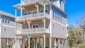 A multi-story beachfront house with a balcony, a porch, and a flag.