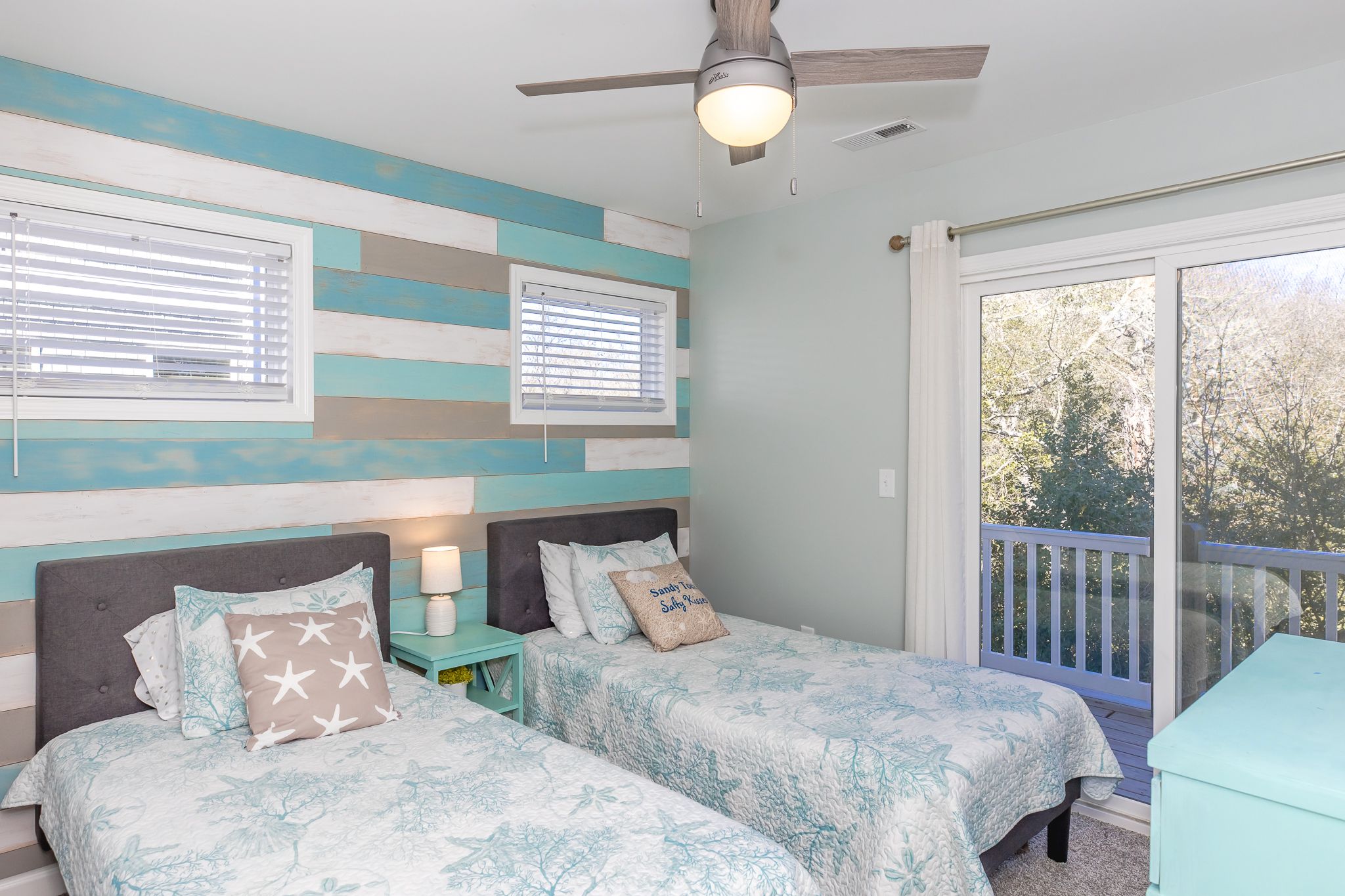 A bedroom with two beds, a ceiling fan, and a view of the outdoors.
