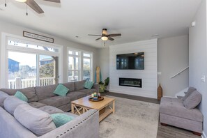 Una sala de estar moderna con sofá, sillón, mesa de centro, televisor, chimenea y ventilador de techo.