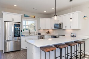 Una cocina moderna con armarios blancos, electrodomésticos de acero inoxidable y una isla central con taburetes de bar.