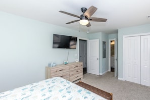 A bedroom with a bed, a dresser, a ceiling fan, a TV, and a door leading to a bathroom.