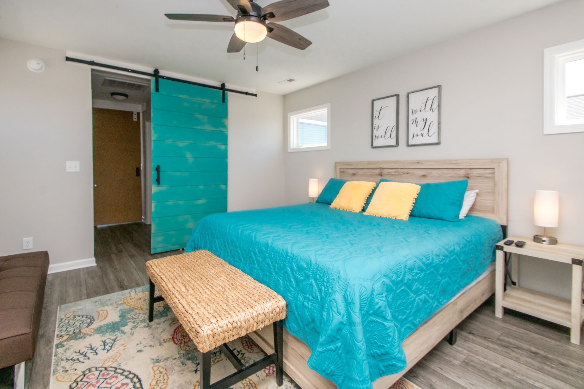 A bedroom with a bed, a bench, a nightstand, a ceiling fan, and a door.