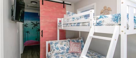 A bunk bed room with a television mounted on the wall, a pink sliding door, and a bed with a 'Good Vibes' pillow.