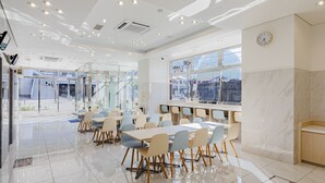 A modern dining area with tables and chairs, large windows, and a clock on the wall. - Toyoko Inn Osaka Dome Mae (Osaka)