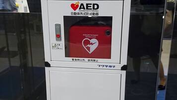 An AED device with a red panel and a heart symbol, labeled in both English and Japanese.