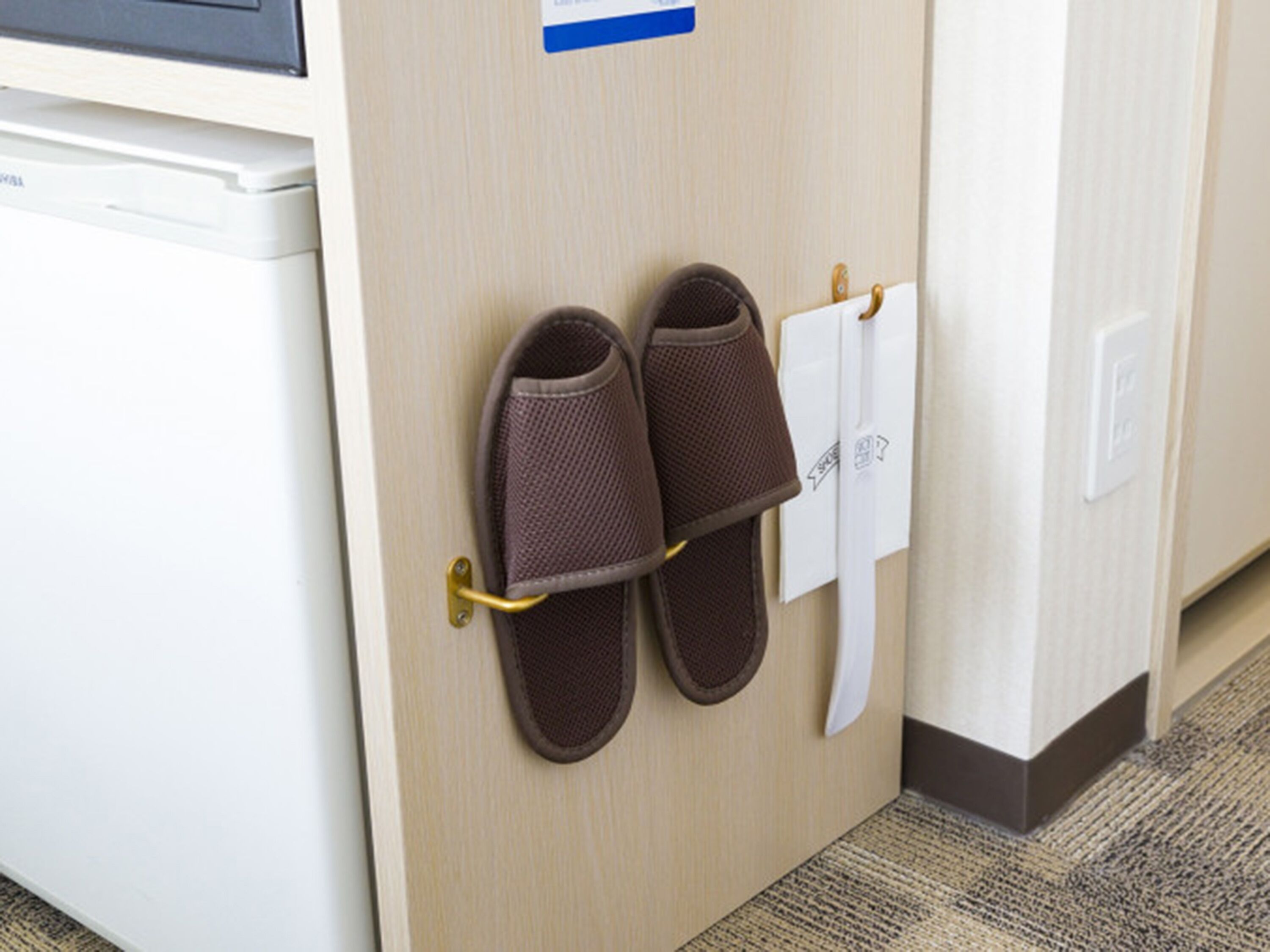 Un par de pantuflas marrones colgadas en un perchero metálico sujeto a una puerta de madera.