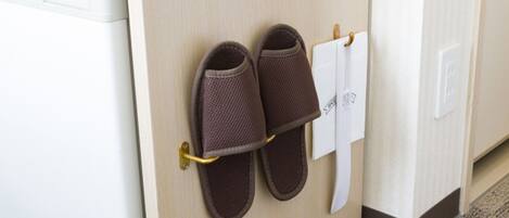 Un par de pantuflas marrones colgadas en un perchero metálico sujeto a una puerta de madera.