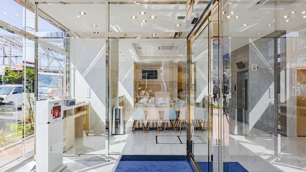 A modern hotel lobby with glass walls, a reception desk, and a seating area with chairs and tables. - Toyoko Inn Osaka Dome Mae (Osaka)