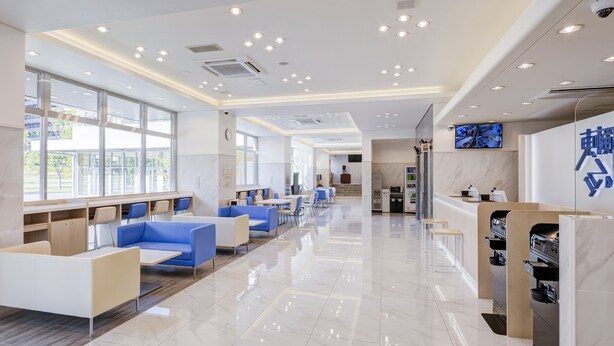 Een moderne hotellobby met een lange receptiebalie, een zithoek met blauwe en witte stoelen, en een automaat.