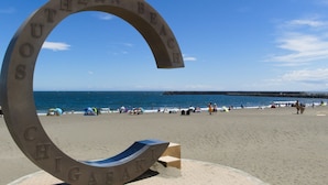 Een gebogen metalen bord met de tekst 'SOUTHERN BEACH CHIGASAKI' op een strand met mensen en tenten.