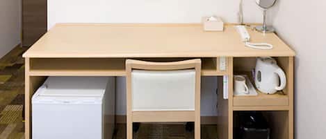 Una habitación pequeña y ordenada con un escritorio de madera, una silla blanca, un refrigerador pequeño, un teléfono, un espejo y un cesto de basura.