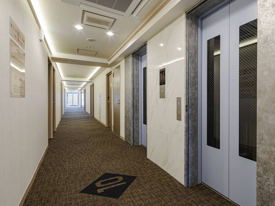 A hotel corridor with a carpeted floor, doors, and a sign indicating room numbers.