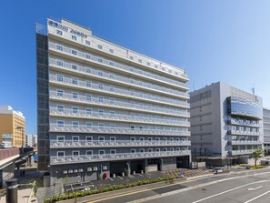 Ein mehrstöckiges Hotel mit modernem Design, mit Balkonen auf jeder Etage und einem Parkplatz vor dem Gebäude.
