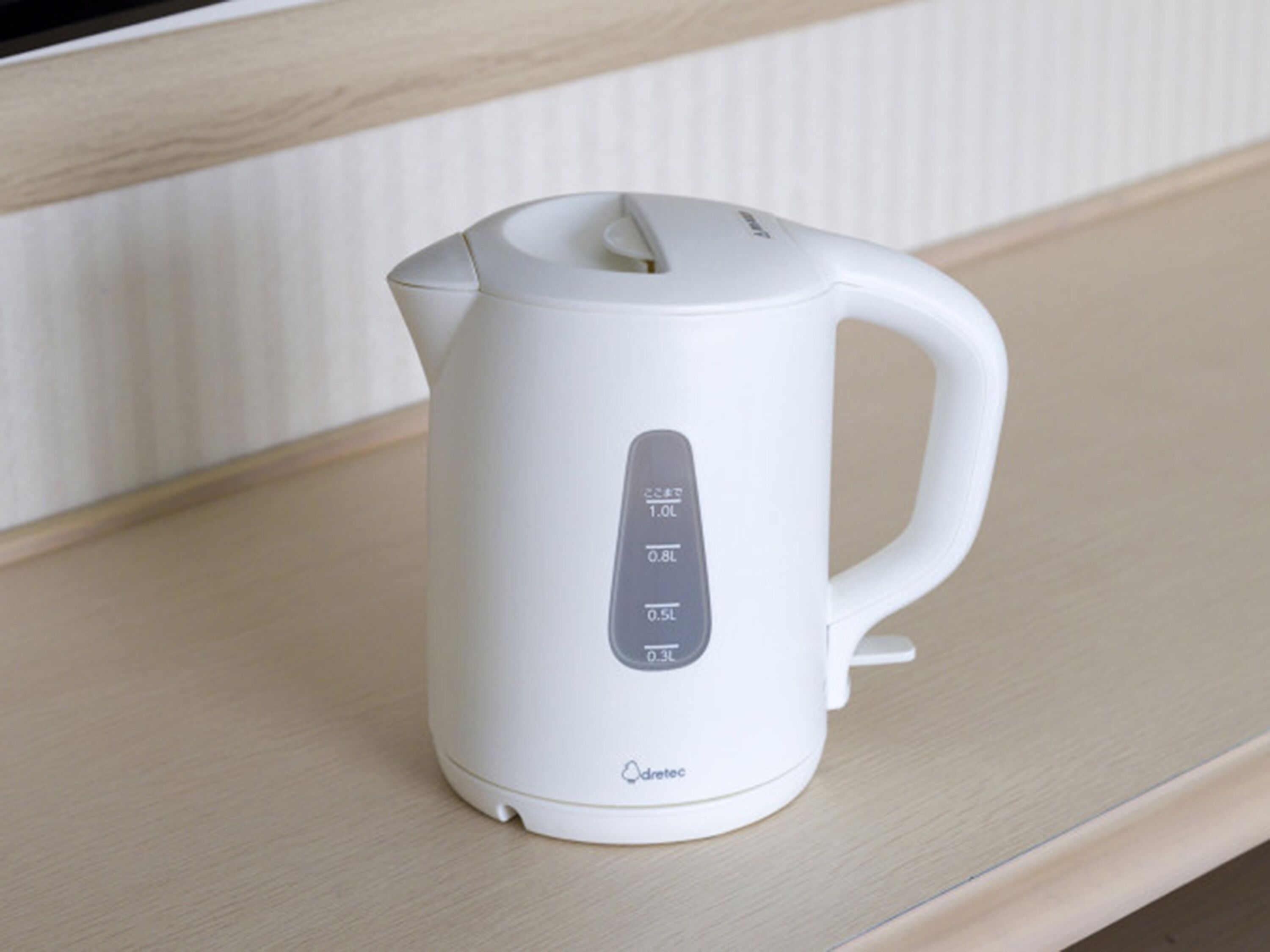 Een witte elektrische waterkoker met maatstrepen op een houten ondergrond.