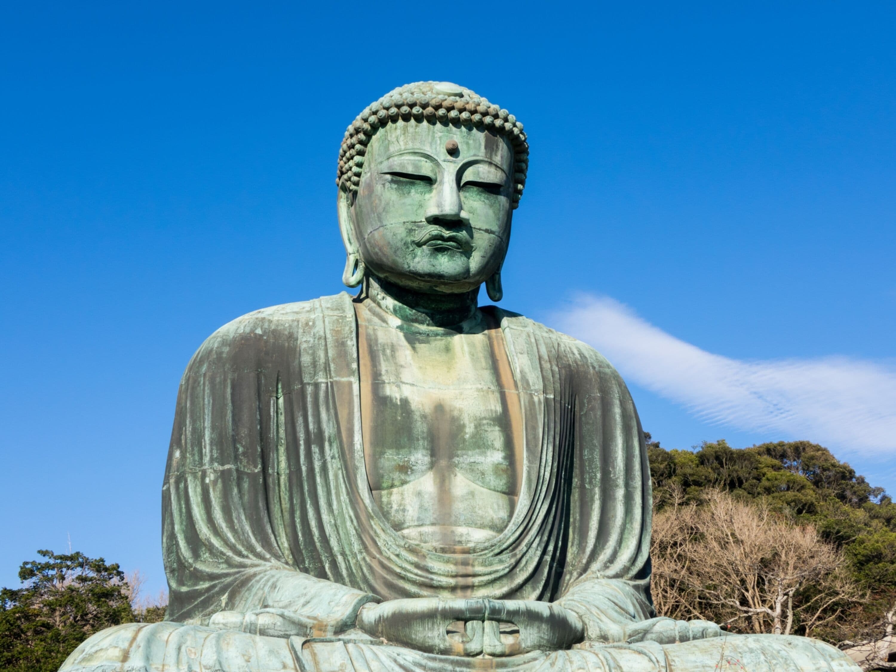 A large bronze Buddha statue with a draped robe, set against a clear blue sky.