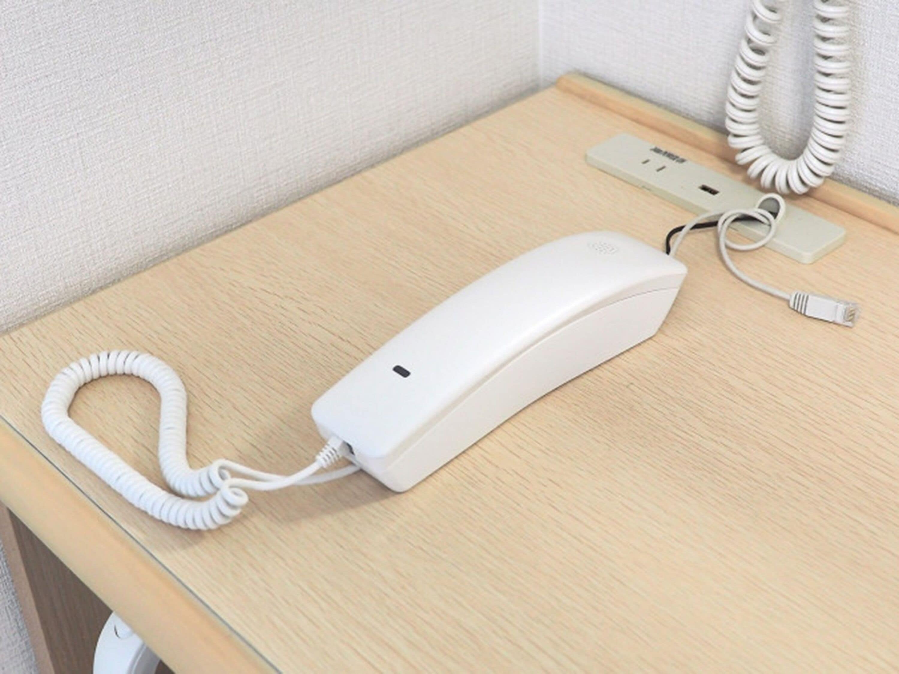 Un téléphone blanc avec un fil enroulé, posé sur une table en bois.