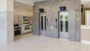 Een moderne lobby met een automaat, een receptiebalie en een glazen lift.