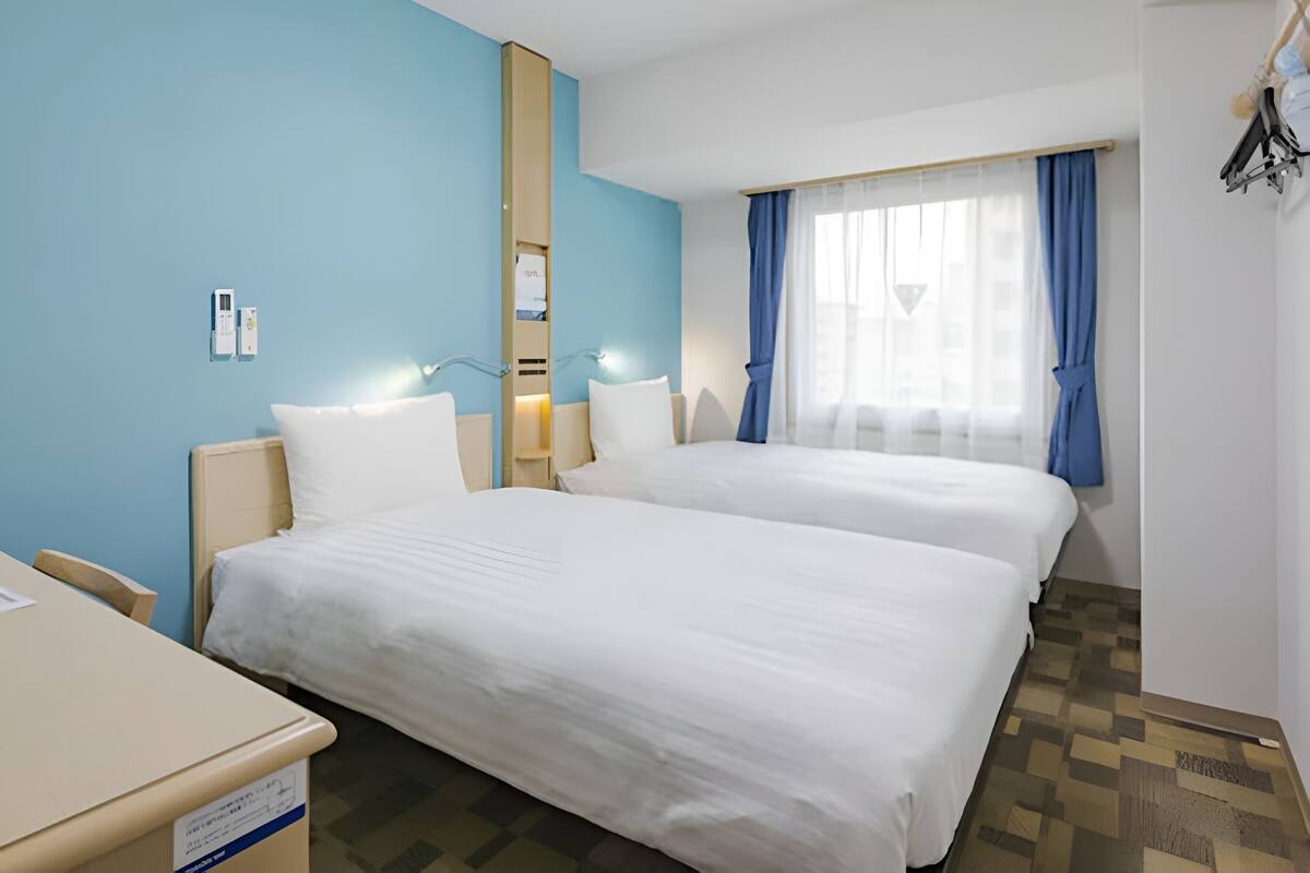 Ein Hotelzimmer mit zwei Betten, einem Schreibtisch, einem Spiegel und einem Fenster mit Vorhängen.